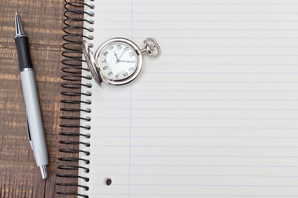 Antique pocket watch on notebook for notes. On textured wood.